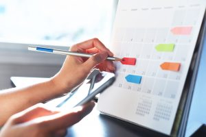 Persons hand placing coloured tags on a calendar for planning a marketing campaign