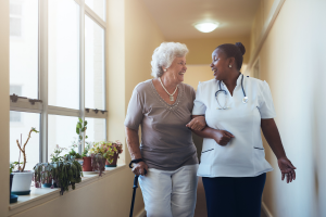 Healthcare provider walking an elderly woman down a hall smiling